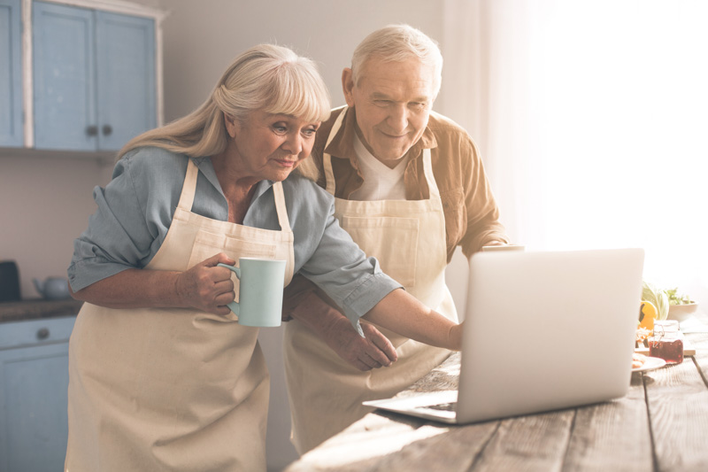 Excited,Senior,Man,And,Woman,Are,Reading,Interesting,Recipe,On Excited senior man and woman are reading interesting recipe on laptop and smiling. They are standing in kitchen and drinking tea. Couple is wearing chef aprons