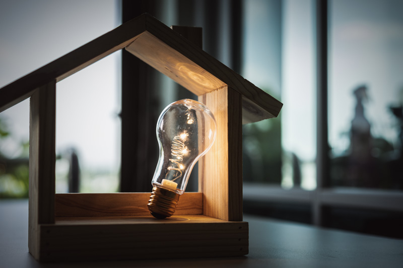 Light,Bulb,With,Wood,House,On,The,Table,,A,Symbol Light bulb with wood house on the table, a symbol for construction, Creative light bulb idea, power energy or business idea concept ecology, loan, mortgage, property or home.